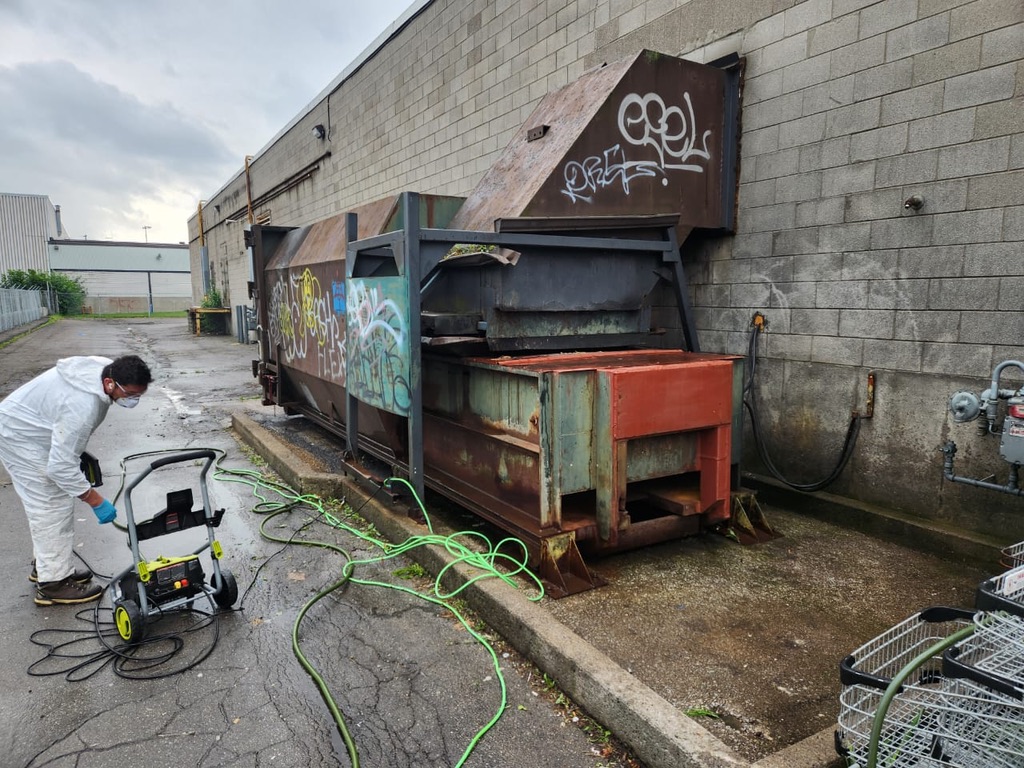 Worker completing the final pressure wash around a cleared commercial compactor