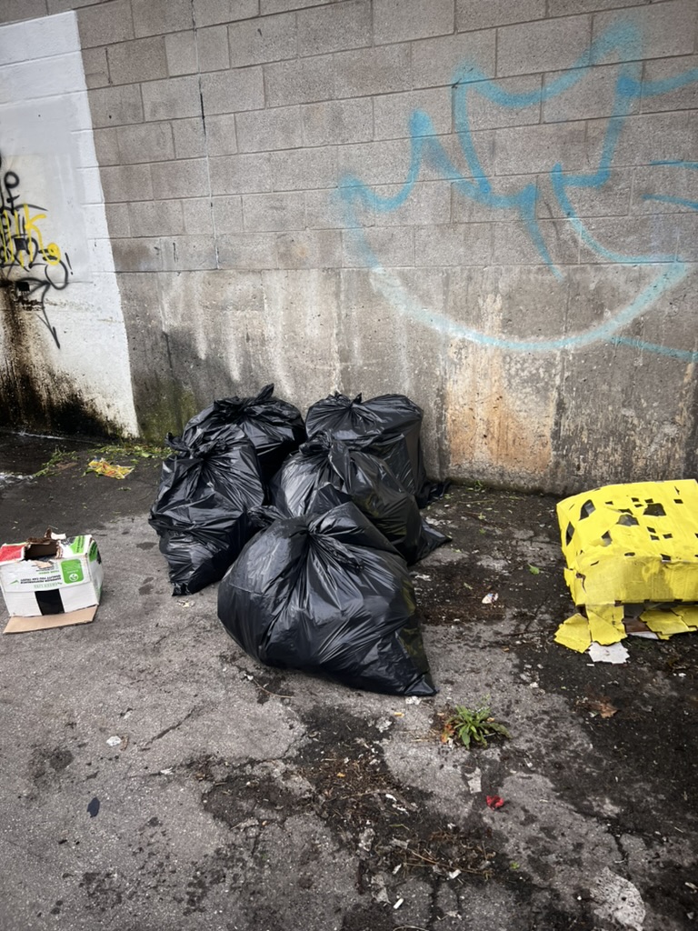 Bagged waste and loose debris beside a commercial facility wall before final cleaning