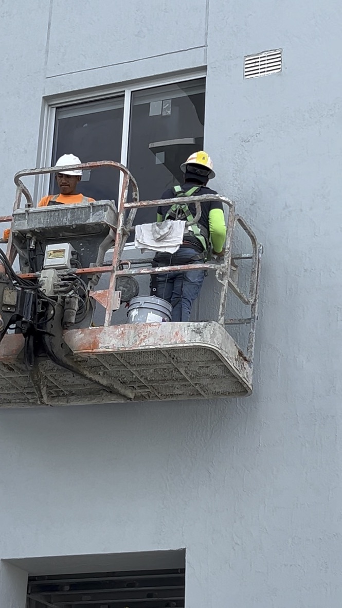 Technicians cleaning an exterior apartment window from elevated equipment